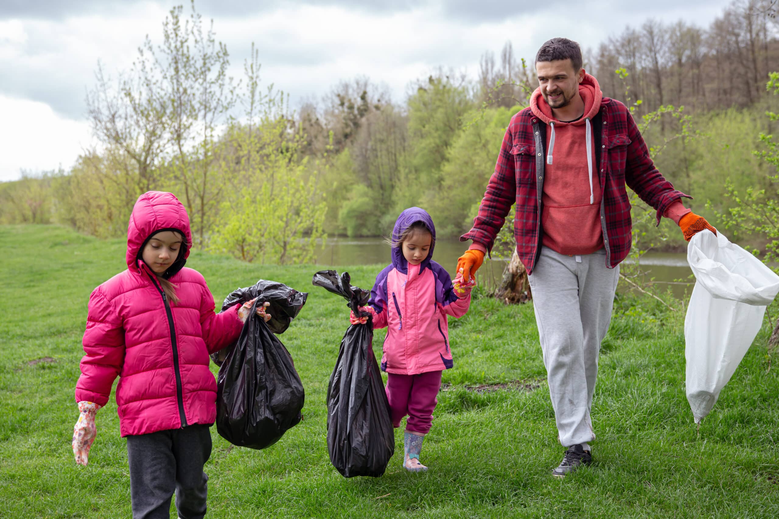 Dad and his little daughters are cleaning the environment in the forest.