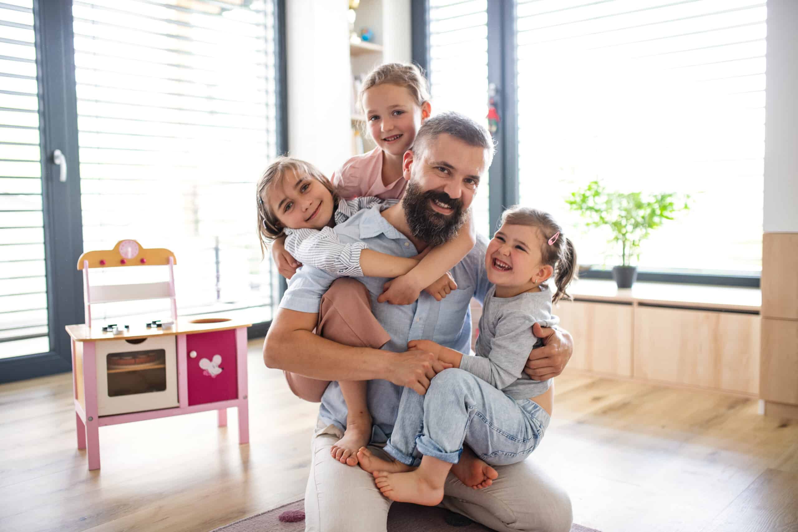Father with three daughters indoors at home, looking at camera.